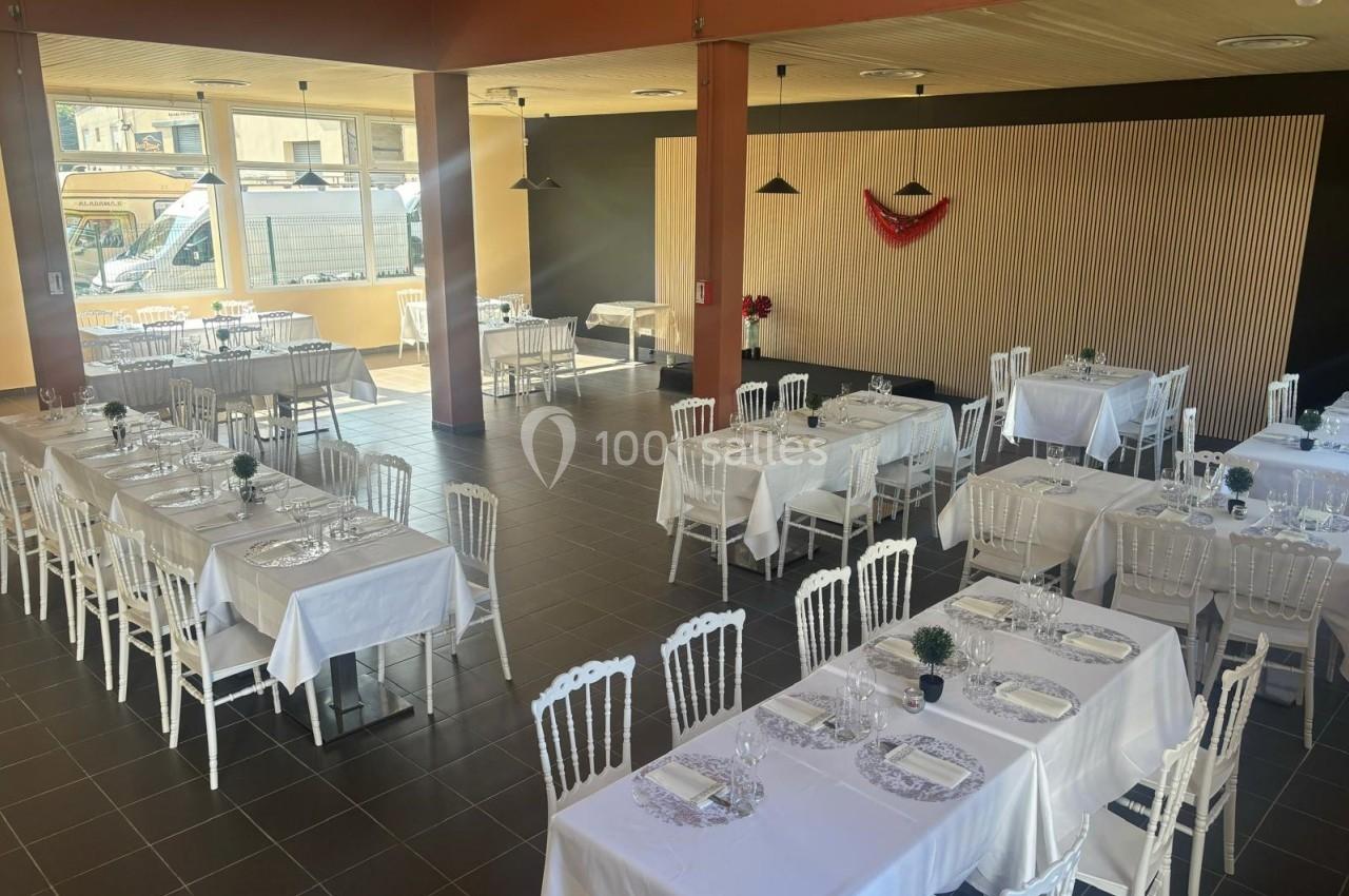Salle de réception lumineuse avec tables dressées, nappes blanches et chaises blanches, décor minimaliste.
