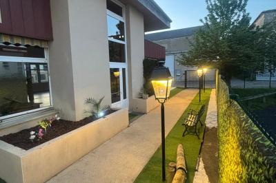 Allée extérieure éclairée par des lampadaires, bordée de bancs, d'arbustes et d'un parterre de fleurs.