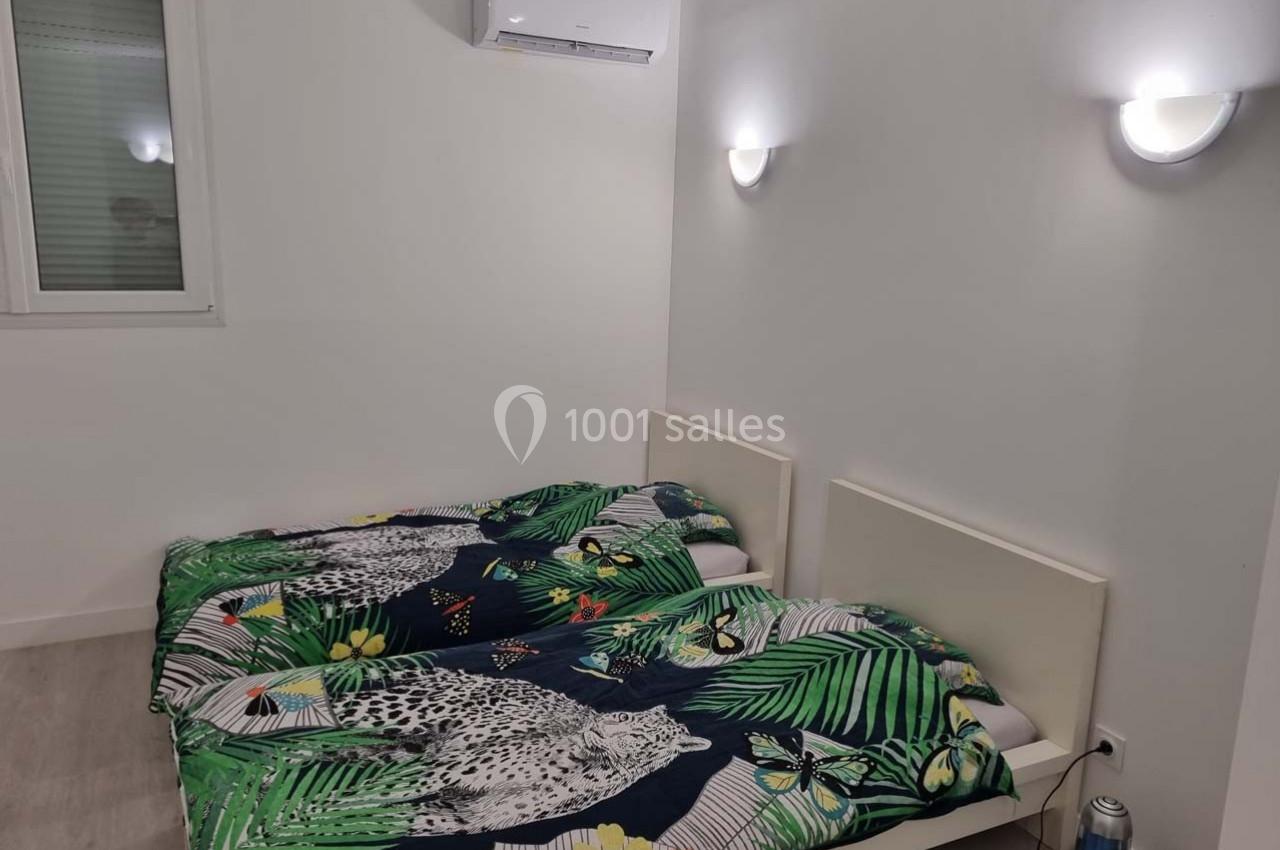 Deux lits simples avec une parure à motifs tropicaux dans une chambre blanche éclairée par des appliques murales.