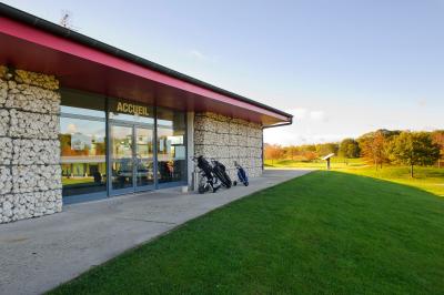 Vue d'un terrain de golf avec des joueurs sur le green, entouré d'arbres et d'un bâtiment en arrière-plan.