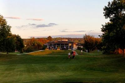Vue d'un terrain de golf avec des joueurs sur le green, entouré d'arbres et d'un bâtiment en arrière-plan.