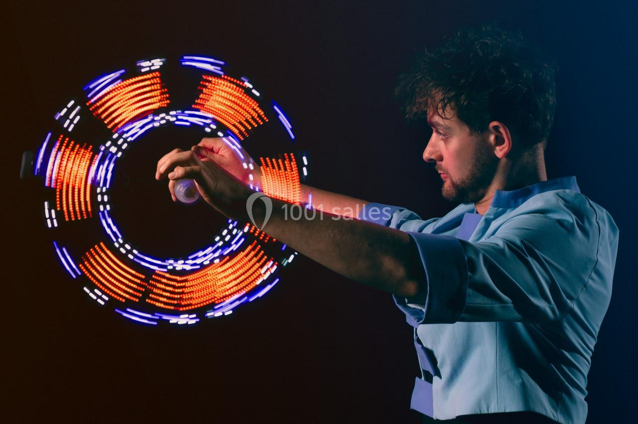 Un homme manipule un objet lumineux créant des motifs circulaires colorés dans un environnement sombre.