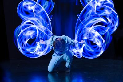 Un jongleur manipule des bâtons rouges dans une galerie lumineuse avec une verrière en arrière-plan.