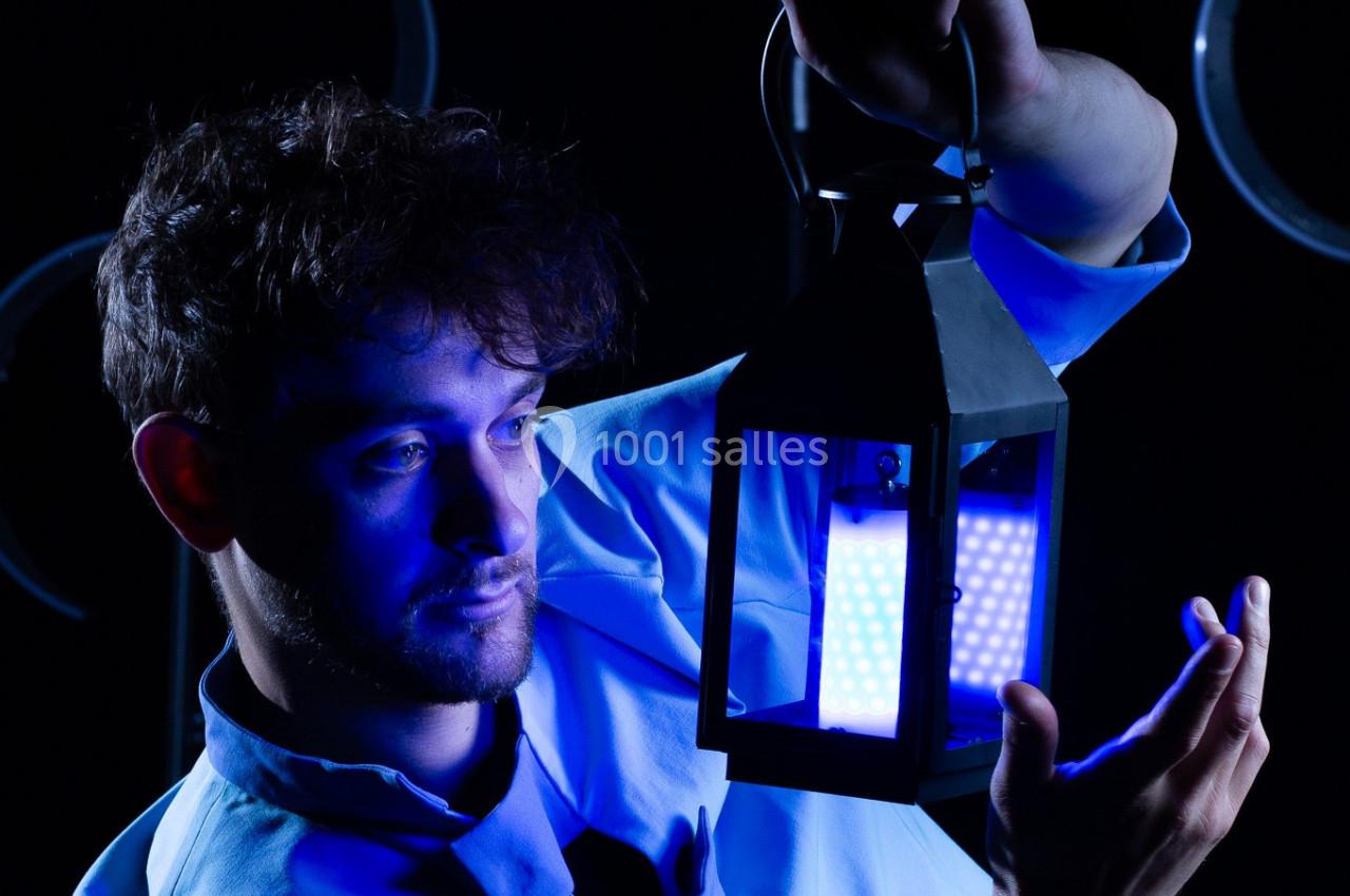 Un homme tenant une lanterne émettant une lumière bleue dans un environnement sombre.
