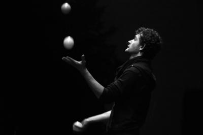 Un jongleur manipule des bâtons rouges dans une galerie lumineuse avec une verrière en arrière-plan.