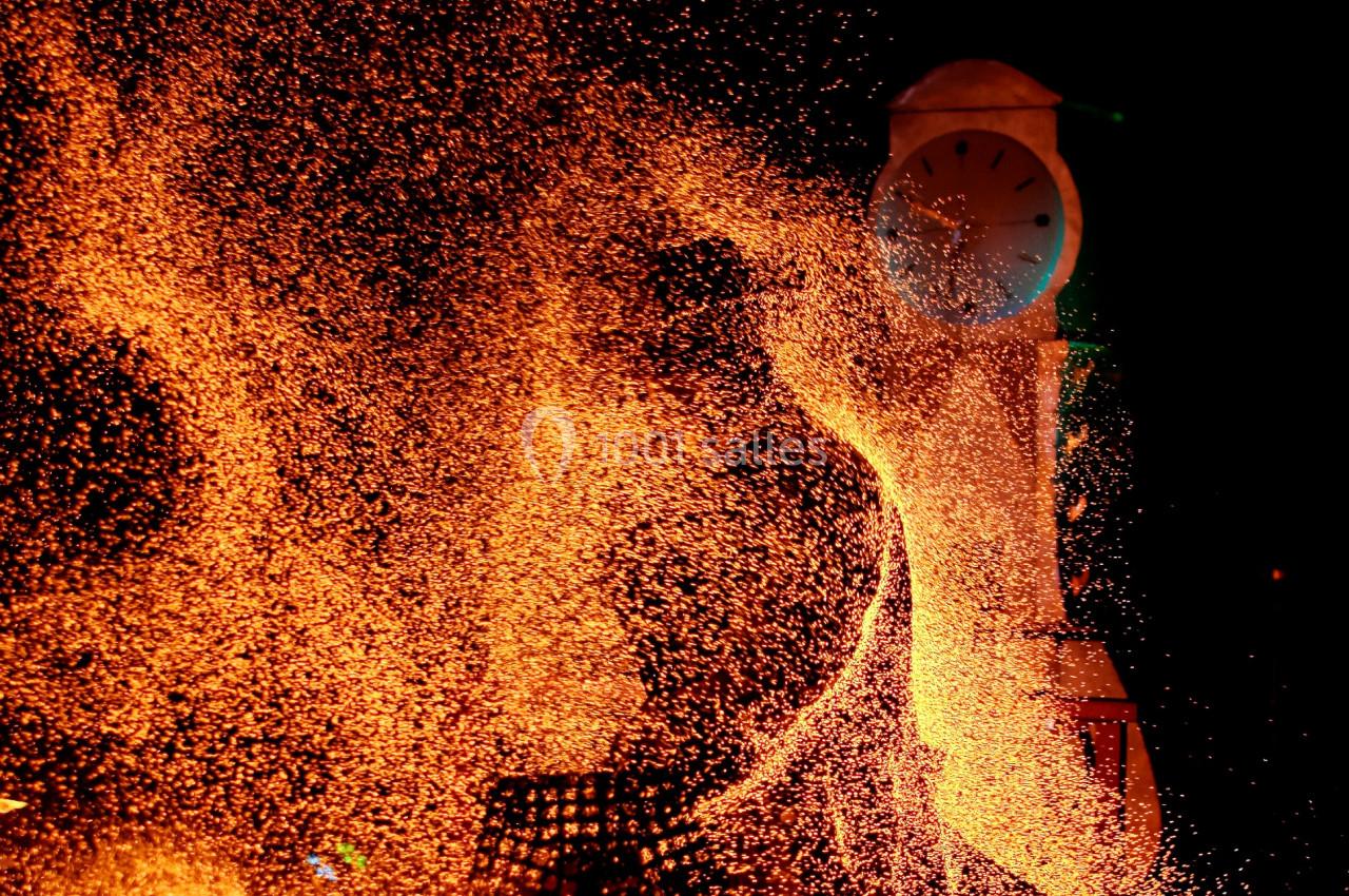 Projection d'étincelles orange devant une horloge illuminée dans l'obscurité.