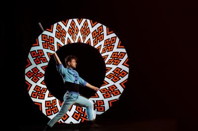 Un jongleur réalise une performance avec des bâtons rouges dans une galerie lumineuse bordée de colonnes.