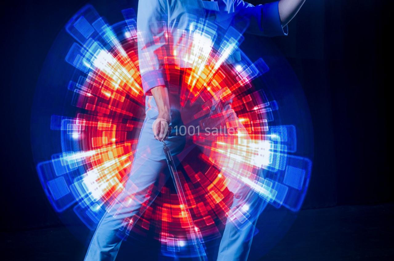 Une personne en tenue claire tient un objet devant un effet lumineux circulaire rouge et bleu en arrière-plan.