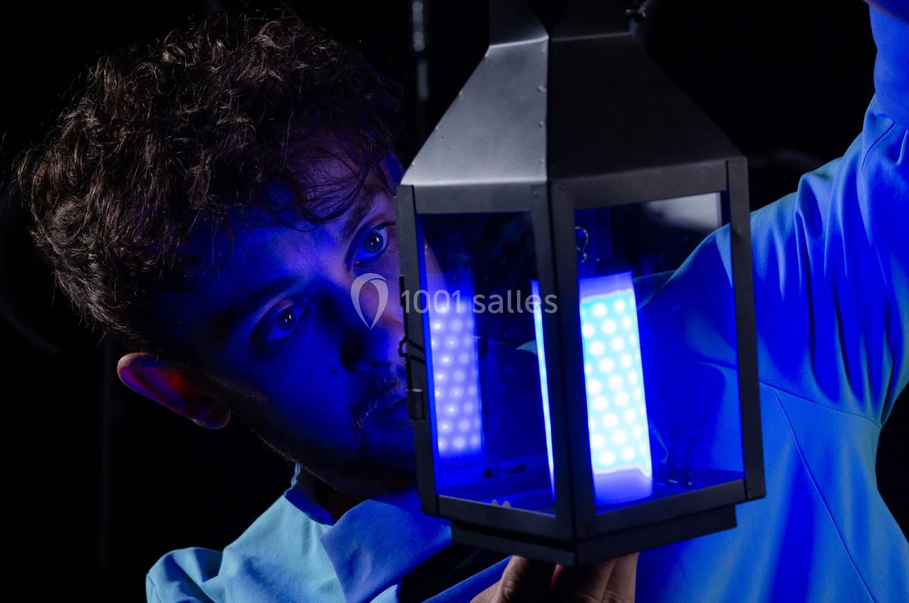 Un homme examine une lanterne émettant une lumière bleue vive dans un environnement sombre.