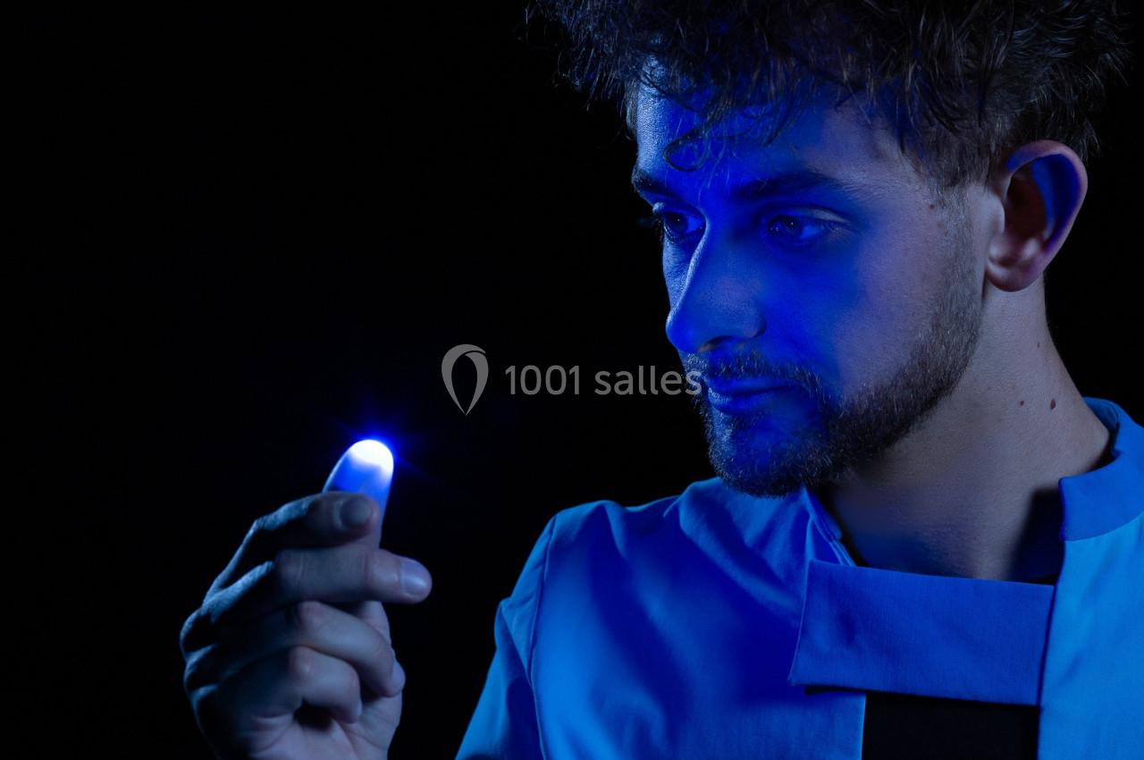 Un homme observe une lumière bleue brillante émanant de son doigt dans un environnement sombre.
