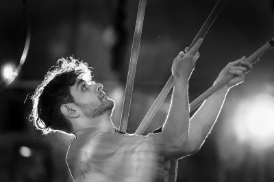 Un jongleur réalise une performance avec des bâtons rouges dans une galerie lumineuse bordée de colonnes.