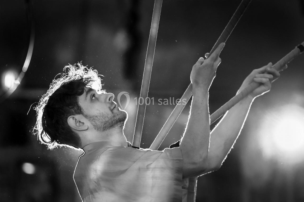 Homme tenant des cordes, regard tourné vers le haut, éclairé par une lumière intense dans un environnement sombre.