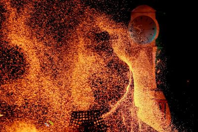 Un jongleur réalise une performance avec des bâtons rouges dans une galerie lumineuse bordée de colonnes.