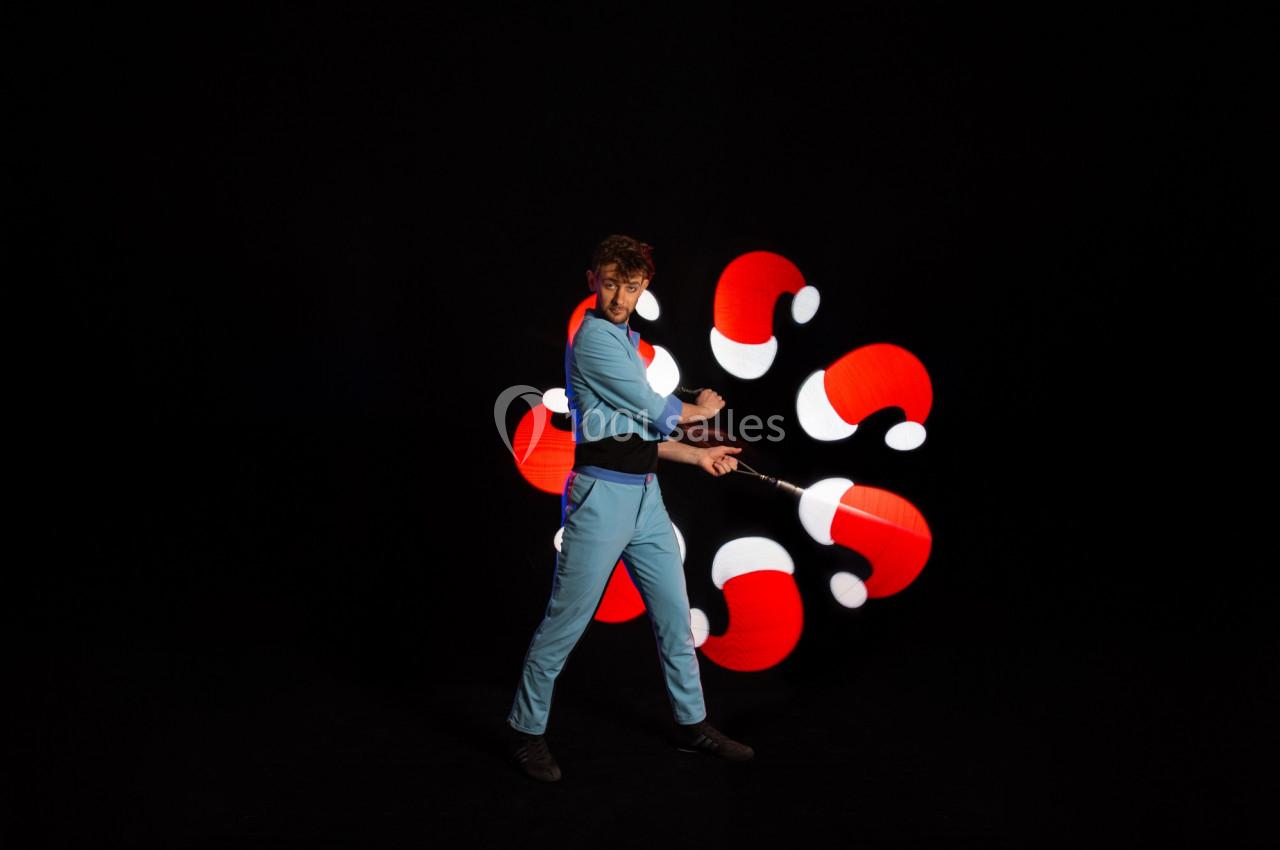 Un homme en tenue bleue manipule un bâton lumineux créant des motifs de chapeaux de Noël sur fond noir.