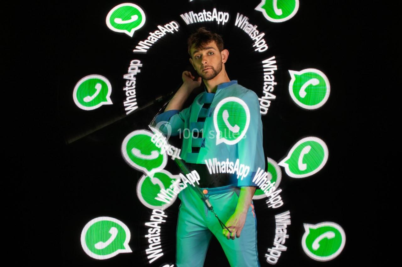 Un homme en tenue bleue pose entouré de logos WhatsApp lumineux sur un fond sombre.