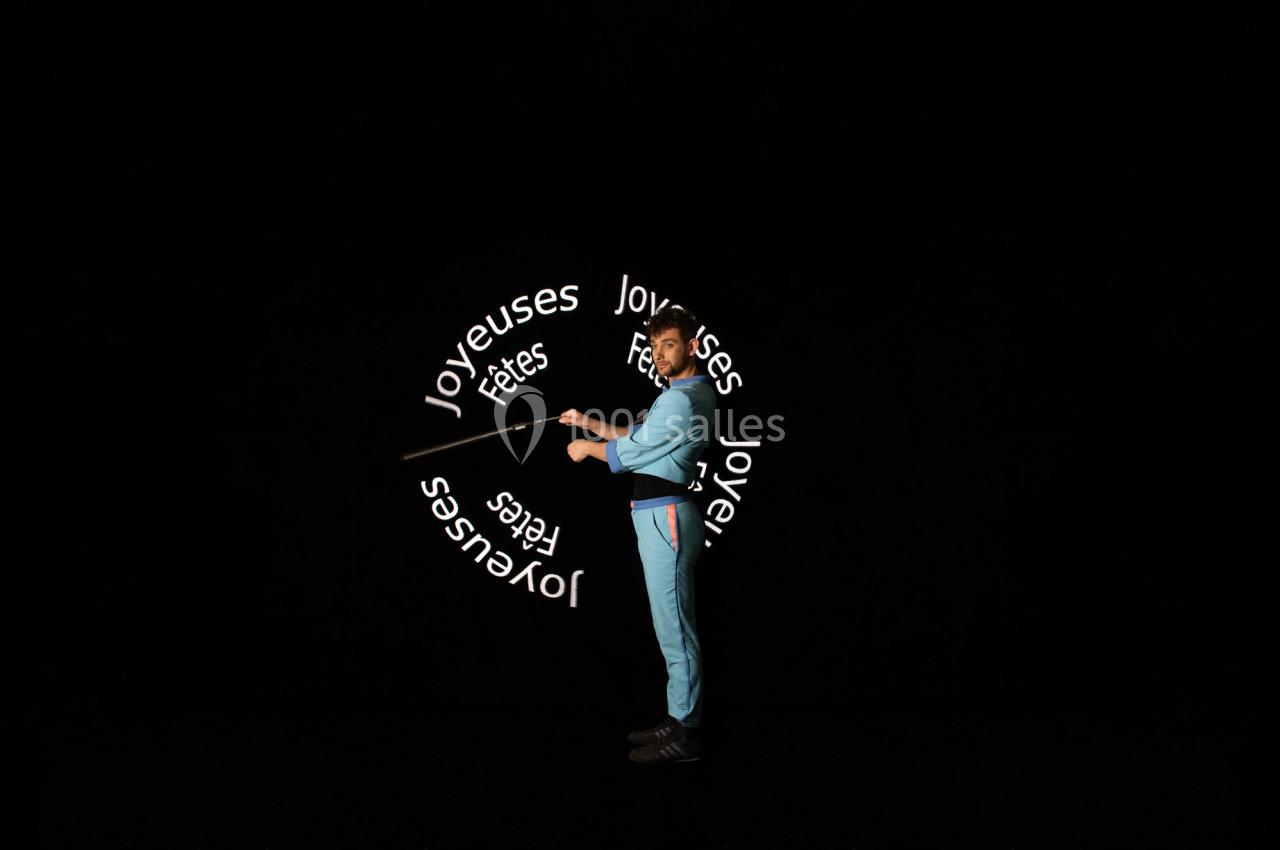 Un homme en tenue bleue manipule un bâton lumineux affichant le message ’Joyeuses fêtes’ sur fond noir.