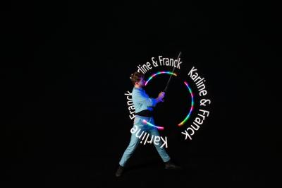 Un jongleur réalise une performance avec des bâtons rouges dans une galerie lumineuse bordée de colonnes.