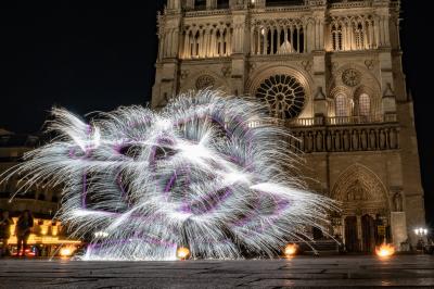 Un jongleur réalise une performance avec des bâtons rouges dans une galerie lumineuse bordée de colonnes.