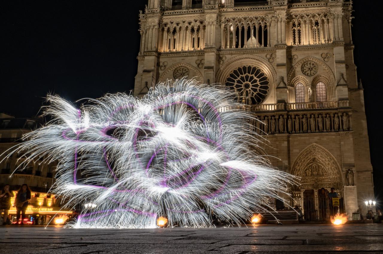 Spectacle de jonglage lumineux devant la cathédrale illuminée de Notre-Dame de Paris, de nuit.