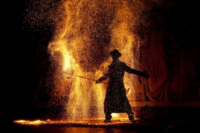 Un jongleur réalise une performance avec des bâtons rouges dans une galerie lumineuse bordée de colonnes.