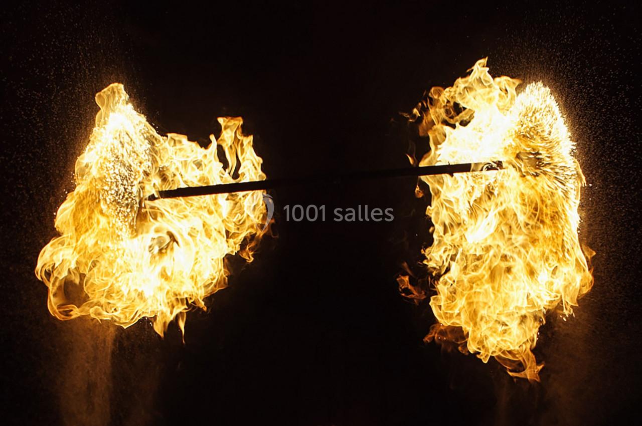 Deux torches enflammées fixées à une barre métallique, entourées d'étincelles et de flammes vives.