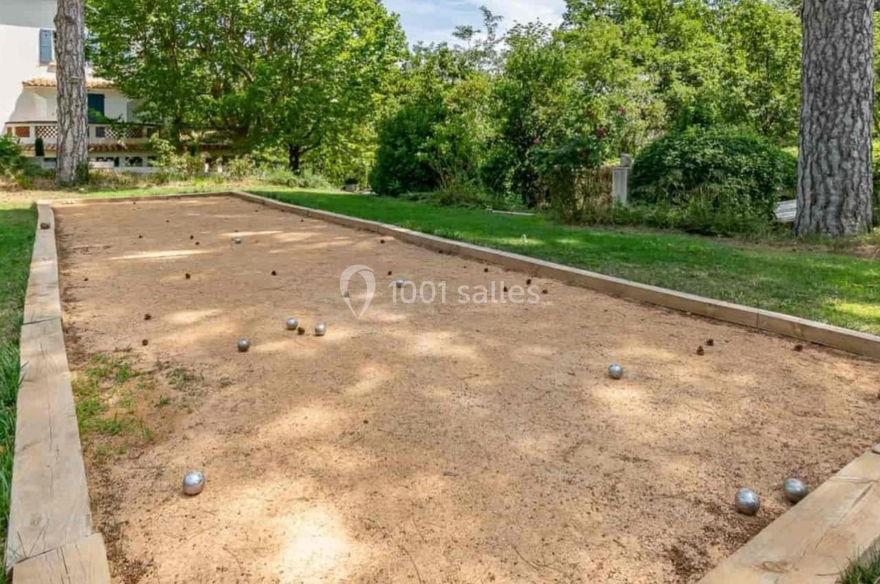 Terrain de pétanque en plein air entouré de verdure, avec des boules dispersées sur le sol sablonneux.