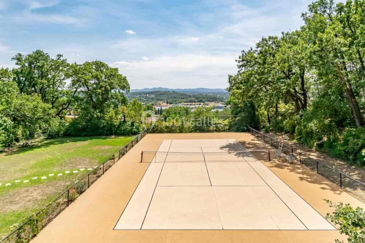 Terrain de tennis en plein air entouré d'arbres et de verdure, avec une vue dégagée sur l'horizon.