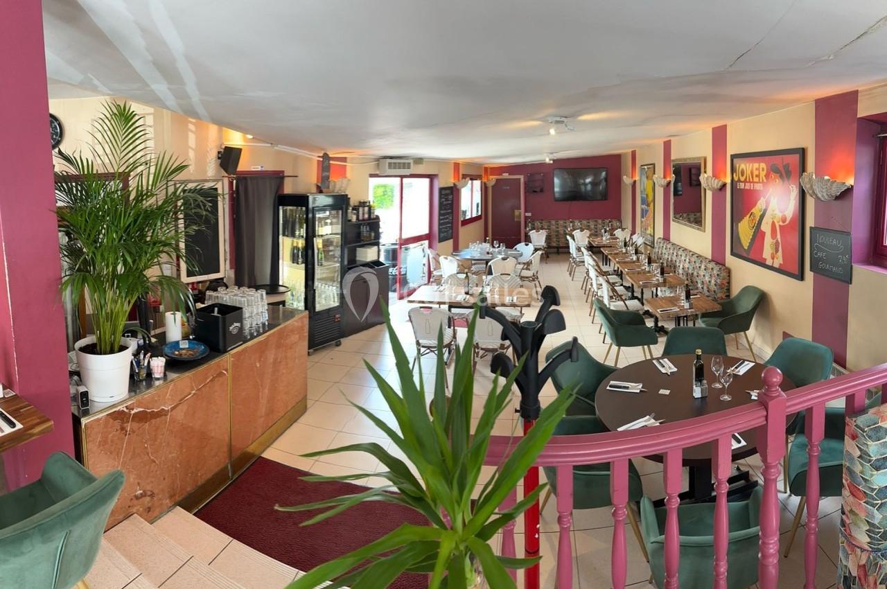 Salle de restaurant lumineuse avec tables dressées, chaises colorées, plantes et décoration murale vive.