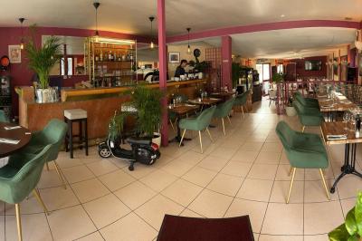 Salle de restaurant lumineuse avec tables dressées, chaises vertes, bar en bois et décoration végétale.