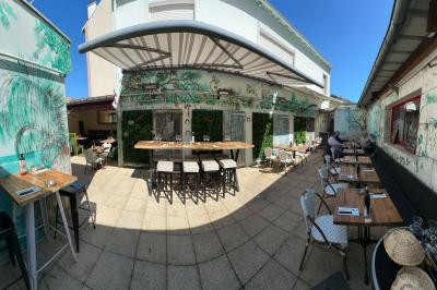 Salle de restaurant lumineuse avec tables dressées, chaises vertes, bar en bois et décoration végétale.