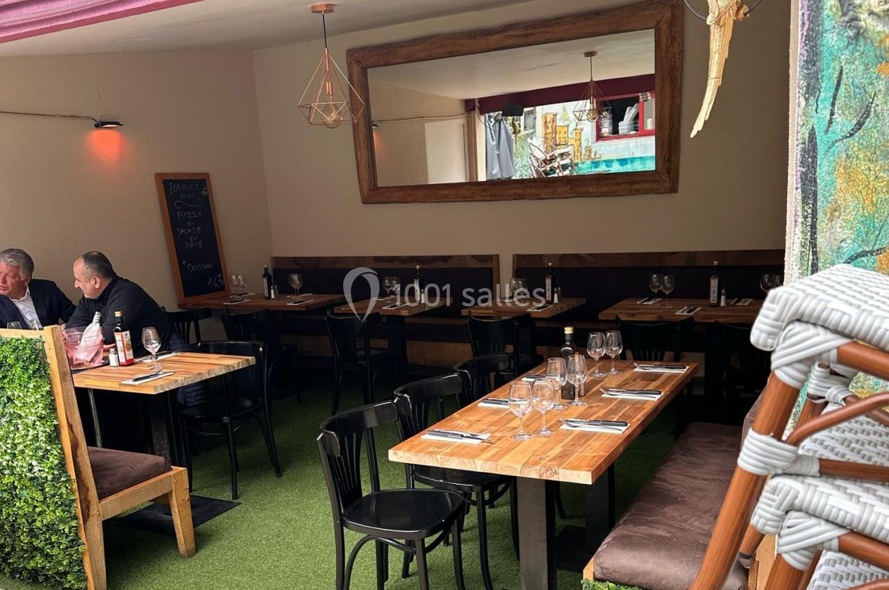 Salle de restaurant avec tables en bois, chaises noires, banquettes brunes, miroir mural et décoration végétale.