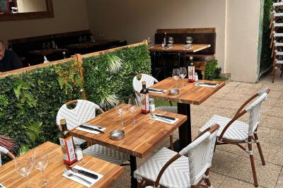 Salle de restaurant lumineuse avec tables dressées, chaises vertes, bar en bois et décoration végétale.