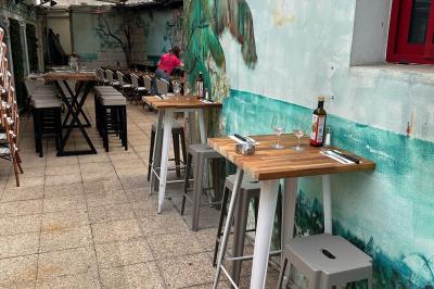 Salle de restaurant lumineuse avec tables dressées, chaises vertes, bar en bois et décoration végétale.