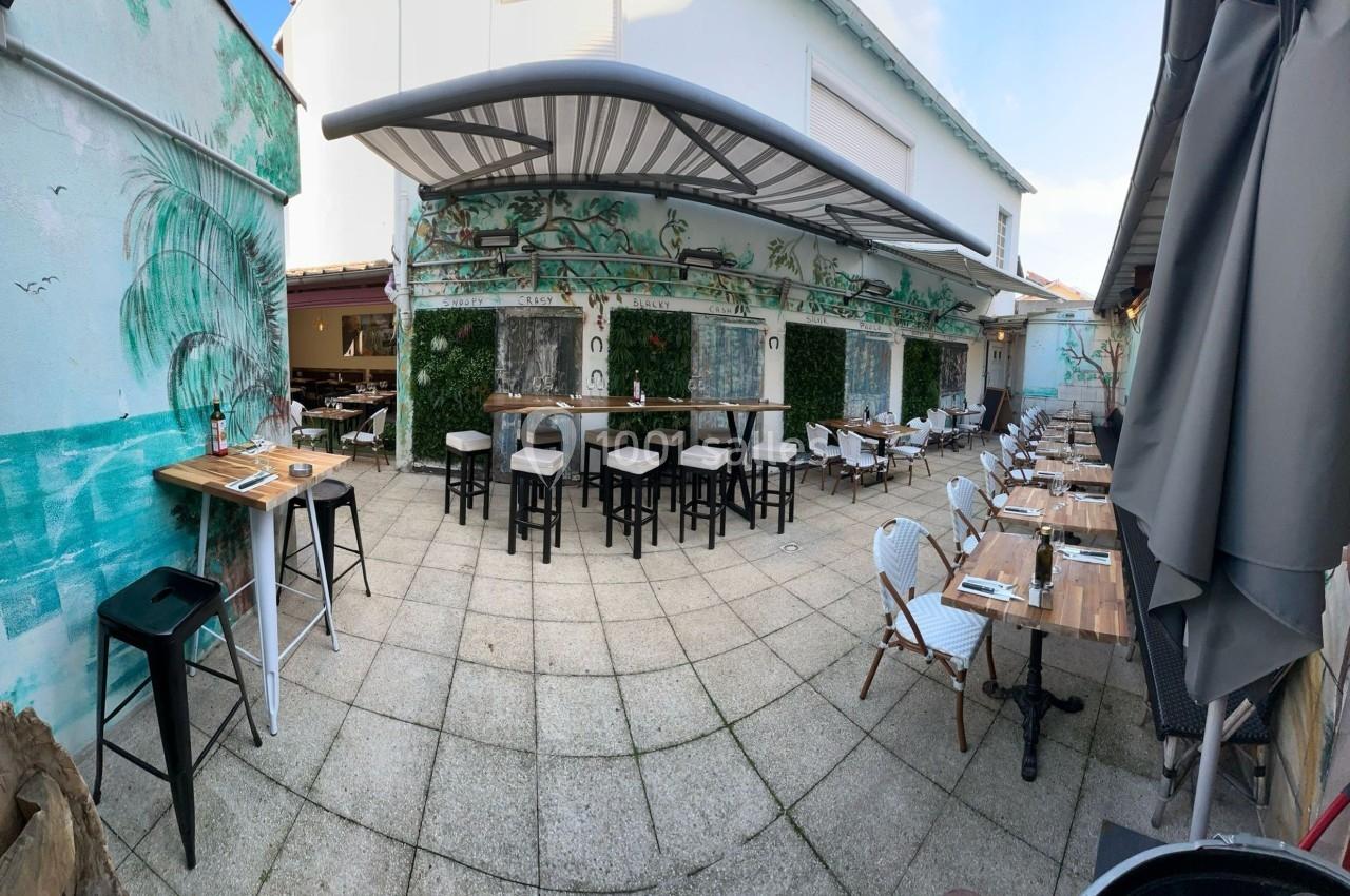 Terrasse extérieure d'un restaurant avec tables, chaises et murs décorés de fresques végétales.
