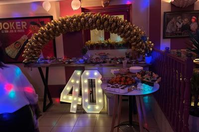 Salle de restaurant lumineuse avec tables dressées, chaises vertes, bar en bois et décoration végétale.