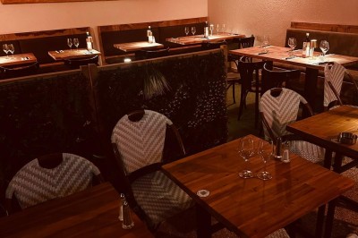 Salle de restaurant lumineuse avec tables en bois, chaises vertes, décorations végétales et comptoir en arrière-plan.