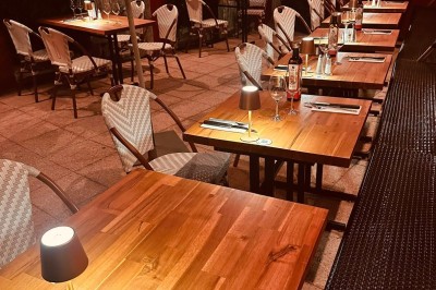 Salle de restaurant lumineuse avec tables en bois, chaises vertes, décorations végétales et comptoir en arrière-plan.