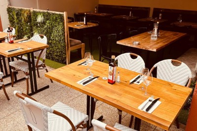 Salle de restaurant lumineuse avec tables en bois, chaises vertes, décorations végétales et comptoir en arrière-plan.