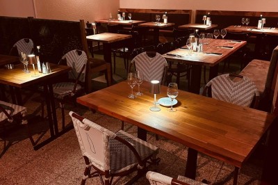 Salle de restaurant lumineuse avec tables en bois, chaises vertes, décorations végétales et comptoir en arrière-plan.