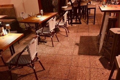 Salle de restaurant lumineuse avec tables en bois, chaises vertes, décorations végétales et comptoir en arrière-plan.