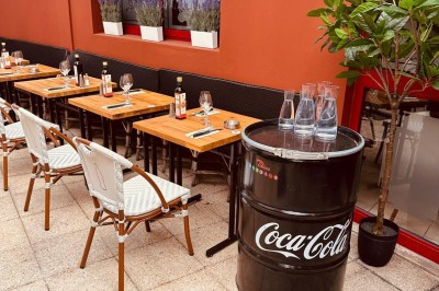 Salle de restaurant lumineuse avec tables en bois, chaises vertes, décorations végétales et comptoir en arrière-plan.