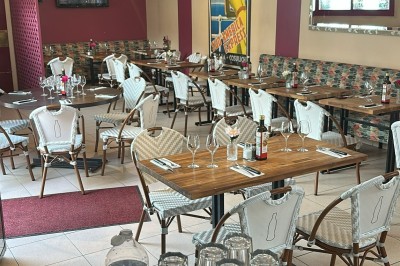 Salle de restaurant lumineuse avec tables en bois, chaises vertes, décorations végétales et comptoir en arrière-plan.