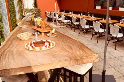 Salle de restaurant lumineuse avec tables en bois, chaises vertes, décorations végétales et comptoir en arrière-plan.
