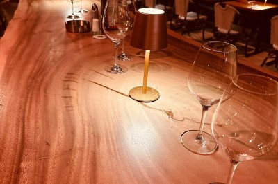 Salle de restaurant lumineuse avec tables en bois, chaises vertes, décorations végétales et comptoir en arrière-plan.