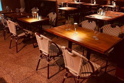 Salle de restaurant lumineuse avec tables en bois, chaises vertes, décorations végétales et comptoir en arrière-plan.