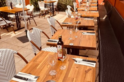 Salle de restaurant lumineuse avec tables en bois, chaises vertes, décorations végétales et comptoir en arrière-plan.