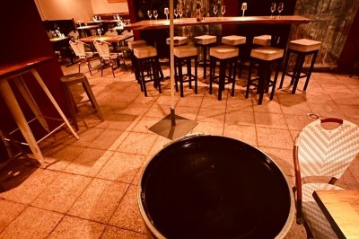Salle de restaurant lumineuse avec tables en bois, chaises vertes, décorations végétales et comptoir en arrière-plan.