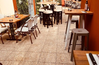 Salle de restaurant lumineuse avec tables en bois, chaises vertes, décorations végétales et comptoir en arrière-plan.