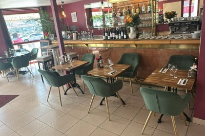 Salle de restaurant lumineuse avec tables en bois, chaises vertes, décorations végétales et comptoir en arrière-plan.