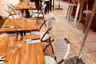 Salle de restaurant lumineuse avec tables en bois, chaises vertes, décorations végétales et comptoir en arrière-plan.